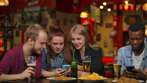A-man-and-two-girls-are-sitting-in-a-bar-and-looking-at-the-phone-screen-while-in-the-company-of-friends.